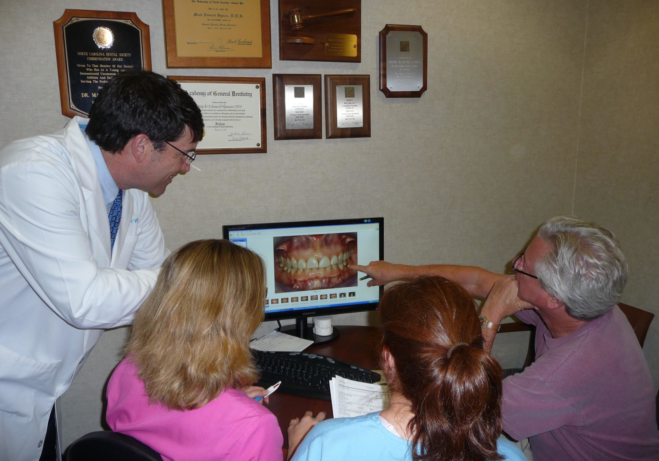 Dr. Hyman showing dental photographs on computer screen to patients in consultation room